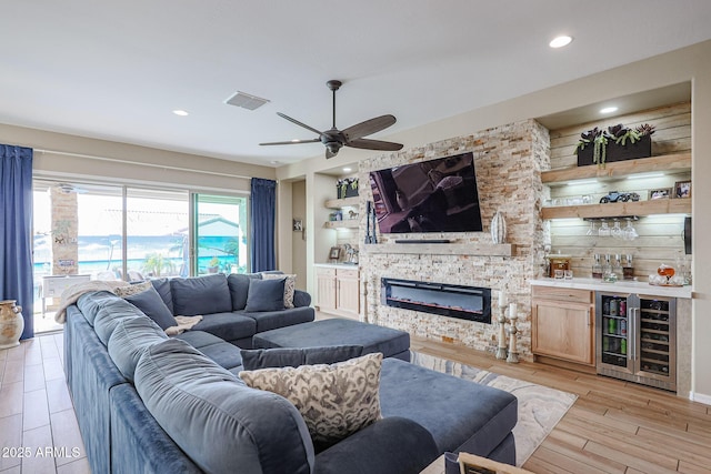 living room with ceiling fan, indoor bar, light hardwood / wood-style flooring, a fireplace, and wine cooler