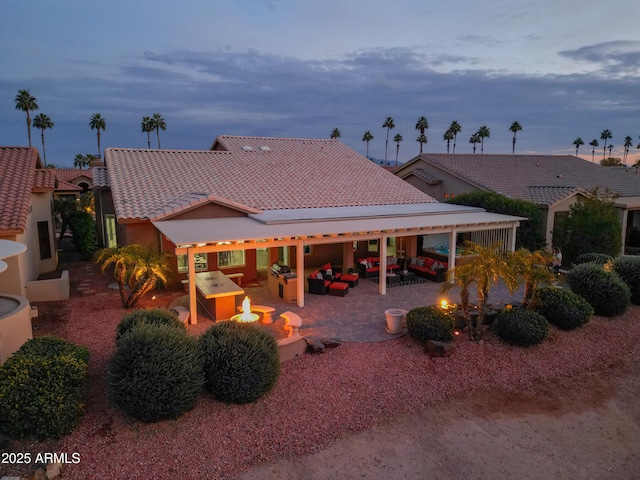 back house at dusk featuring a patio area and an outdoor living space with a fire pit