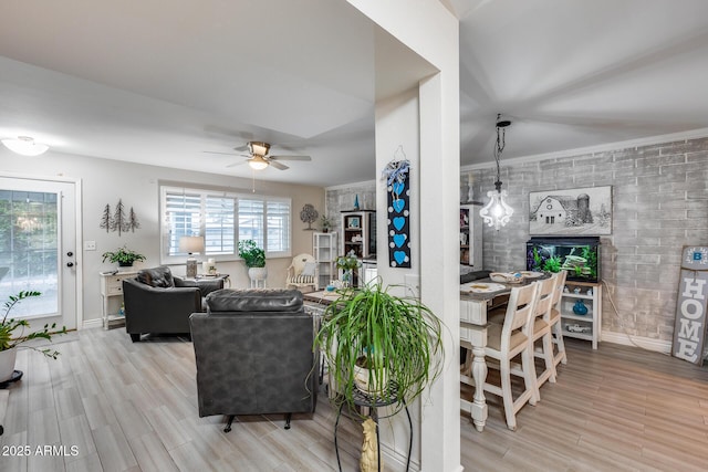 living area with a fireplace, baseboards, ceiling fan, and wood finished floors