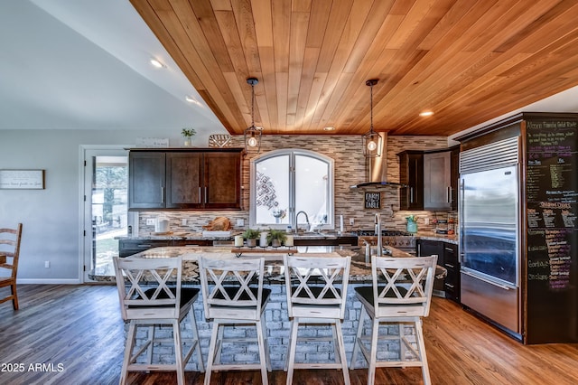 kitchen with stainless steel built in refrigerator, a center island, light stone countertops, pendant lighting, and wood ceiling