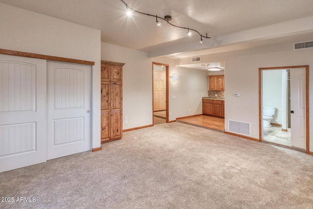 unfurnished bedroom featuring ensuite bath, rail lighting, a closet, and light carpet