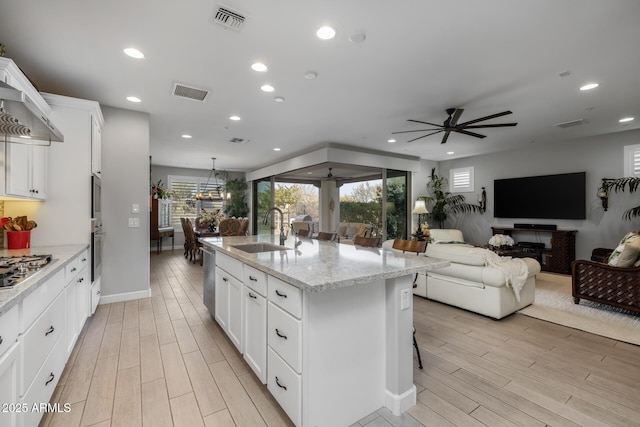 kitchen with a breakfast bar, a kitchen island with sink, sink, and white cabinets