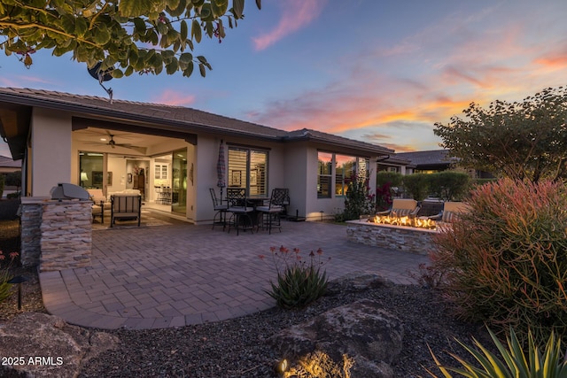 back house at dusk with a patio, an outdoor kitchen, ceiling fan, and an outdoor fire pit