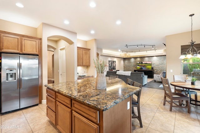 kitchen featuring a breakfast bar, light tile patterned floors, hanging light fixtures, a center island, and stainless steel fridge