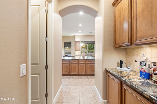 bar with dark stone countertops, backsplash, and light tile patterned floors