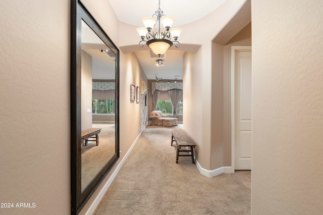 hallway with light colored carpet and a notable chandelier