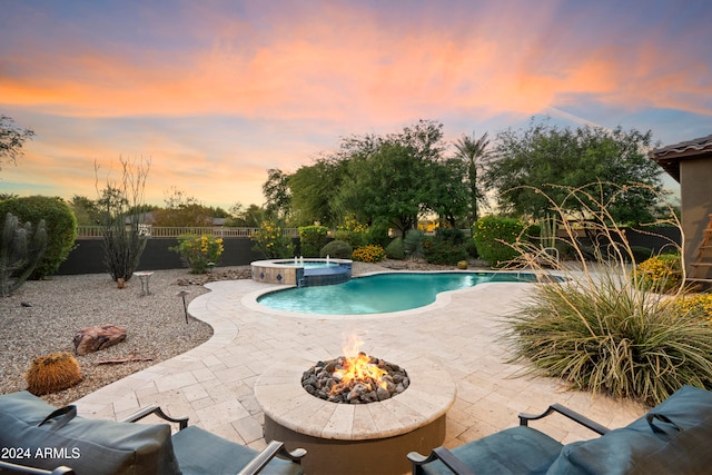 pool at dusk featuring a patio, a fire pit, and an in ground hot tub