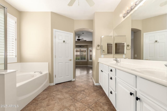 full bath featuring double vanity, a garden tub, ceiling fan, and a sink