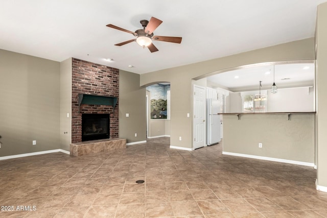 unfurnished living room featuring baseboards, arched walkways, a brick fireplace, and a ceiling fan