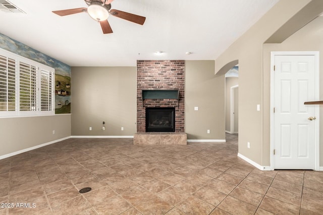 unfurnished living room featuring visible vents, arched walkways, baseboards, a brick fireplace, and ceiling fan