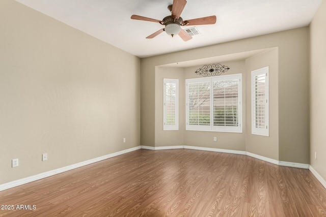 empty room with visible vents, a ceiling fan, baseboards, and wood finished floors