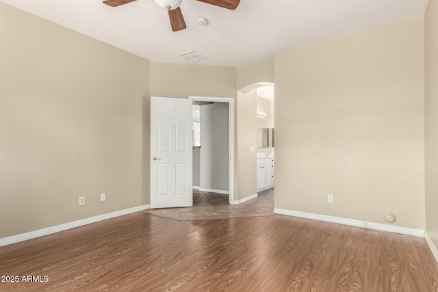 unfurnished bedroom featuring visible vents, wood finished floors, arched walkways, and baseboards