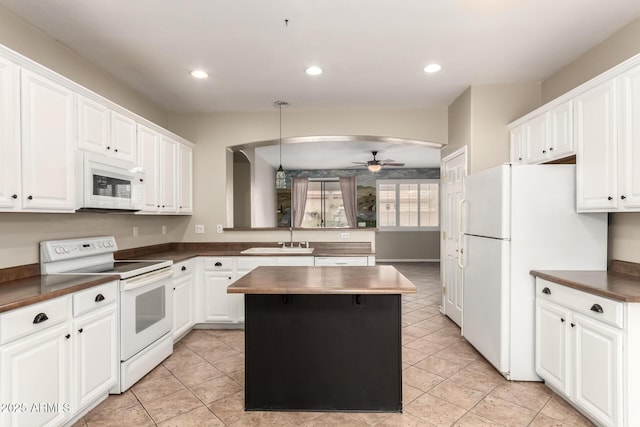 kitchen featuring a sink, dark countertops, a kitchen island, white appliances, and ceiling fan