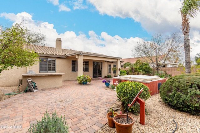 back of house with a chimney, a patio area, a tiled roof, and a hot tub