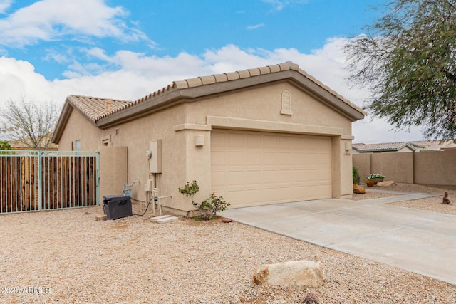 view of side of property with stucco siding, driveway, fence, a garage, and a tiled roof