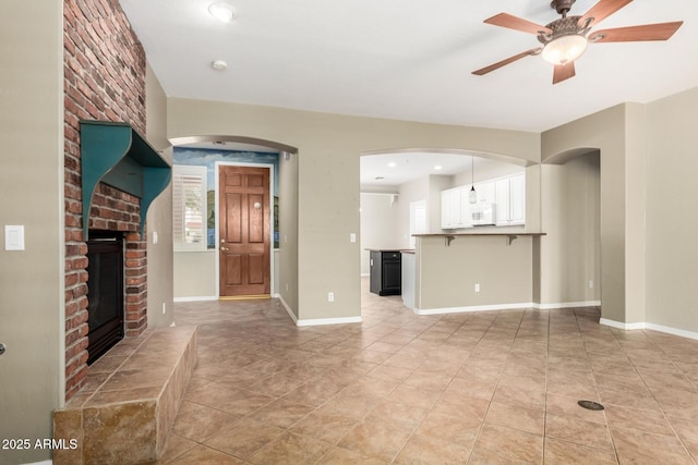 unfurnished living room featuring light tile patterned floors, baseboards, a brick fireplace, and ceiling fan