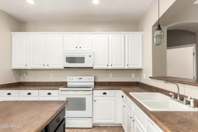 kitchen featuring dark countertops, white cabinets, white appliances, and a sink