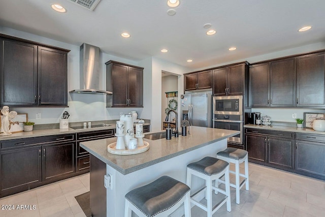 kitchen with a kitchen breakfast bar, stainless steel appliances, sink, wall chimney range hood, and a center island with sink