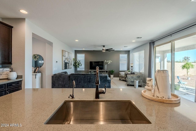 kitchen with ceiling fan, light stone counters, dark brown cabinetry, and sink