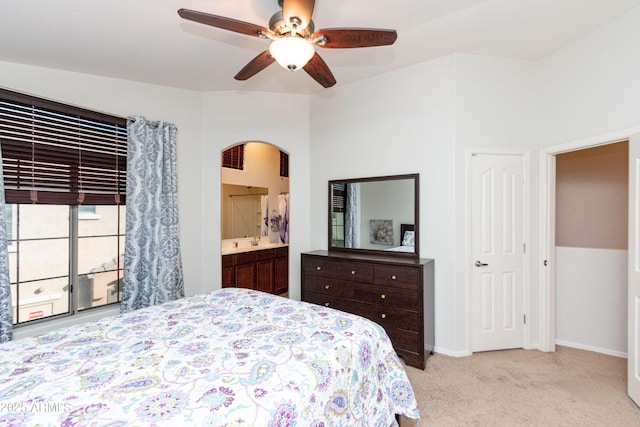 bedroom featuring ceiling fan, ensuite bathroom, arched walkways, light colored carpet, and baseboards