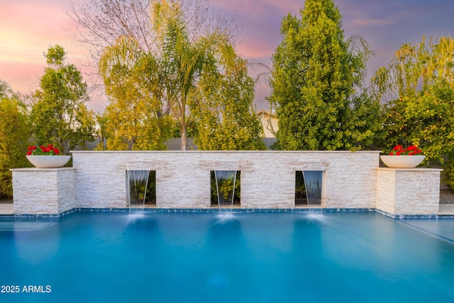 pool at dusk featuring pool water feature