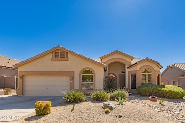 mediterranean / spanish-style home with a tile roof, driveway, an attached garage, and stucco siding