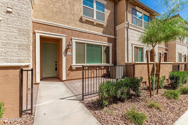 view of exterior entry with fence and stucco siding