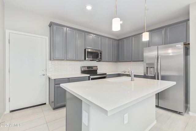 kitchen with hanging light fixtures, a sink, stainless steel appliances, gray cabinetry, and backsplash