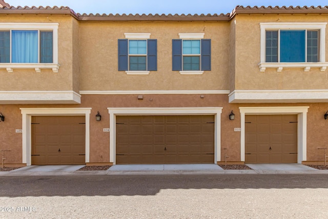 multi unit property with an attached garage, a tile roof, and stucco siding