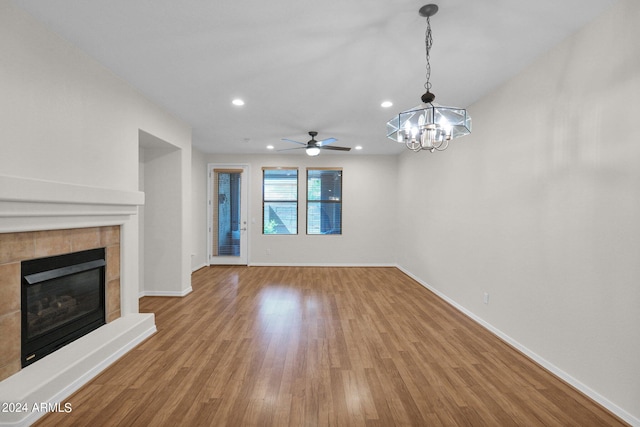 unfurnished living room with ceiling fan with notable chandelier, light wood-type flooring, and a tiled fireplace