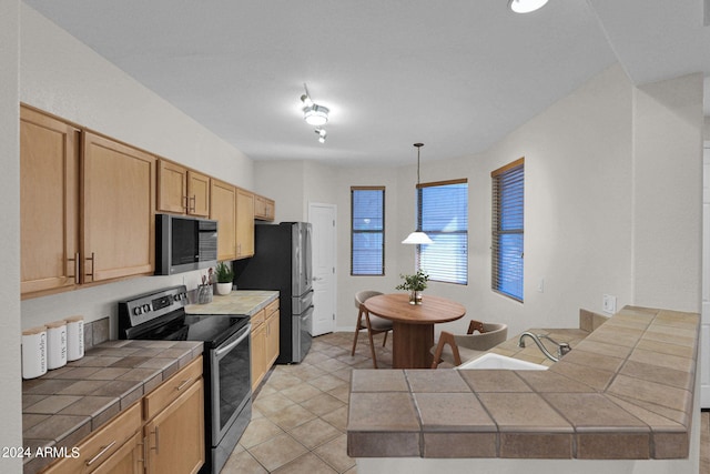 kitchen with tile counters, appliances with stainless steel finishes, light tile patterned floors, decorative light fixtures, and light brown cabinetry