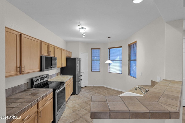 kitchen with tile counters, sink, appliances with stainless steel finishes, light tile patterned floors, and decorative light fixtures