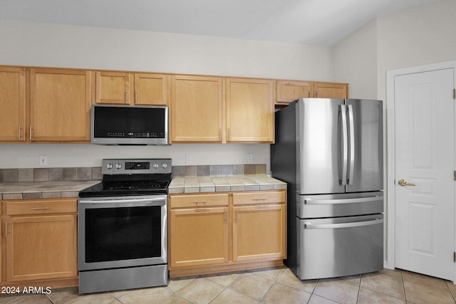 kitchen with appliances with stainless steel finishes, light brown cabinetry, light tile patterned floors, and tile countertops