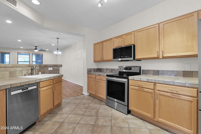 kitchen featuring light tile patterned flooring, stainless steel appliances, tile countertops, light brown cabinetry, and sink