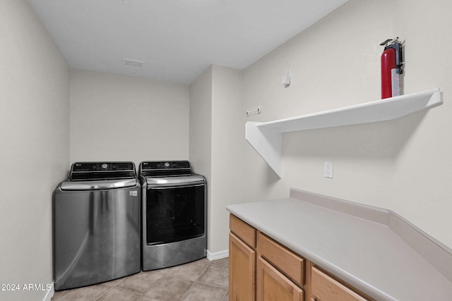 clothes washing area with cabinets, light tile patterned floors, and washing machine and dryer