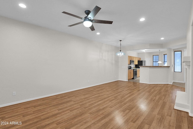 unfurnished living room with light wood-type flooring and ceiling fan with notable chandelier