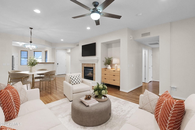 living room with light hardwood / wood-style flooring, a tiled fireplace, and ceiling fan with notable chandelier