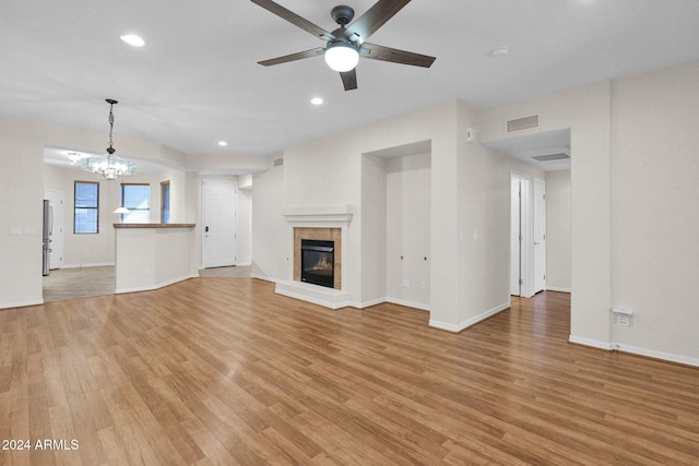 unfurnished living room featuring a tile fireplace, ceiling fan with notable chandelier, and light hardwood / wood-style flooring