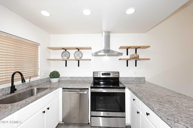 kitchen featuring appliances with stainless steel finishes, white cabinets, sink, light stone countertops, and wall chimney exhaust hood