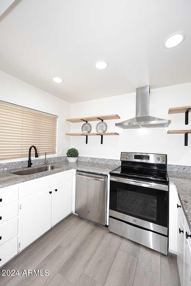 kitchen featuring white cabinetry, wall chimney range hood, stainless steel appliances, light wood-type flooring, and sink