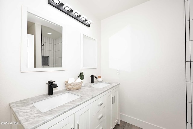 full bath with double vanity, a sink, baseboards, and wood finished floors