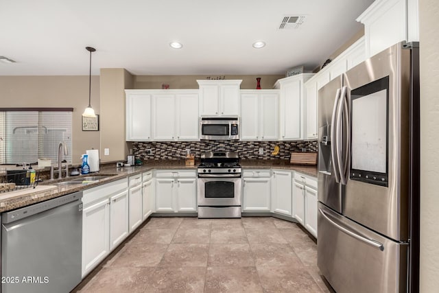 kitchen with stainless steel appliances, dark stone counters, hanging light fixtures, white cabinets, and sink