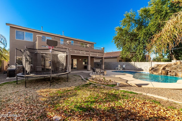 rear view of house featuring a trampoline, a fenced in pool, a balcony, and a patio