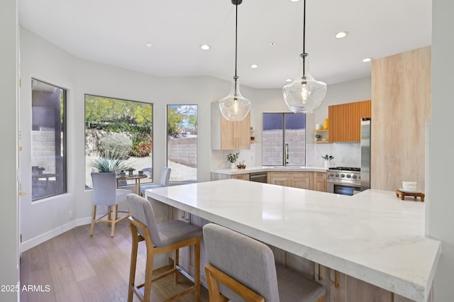 kitchen with appliances with stainless steel finishes, pendant lighting, a kitchen breakfast bar, kitchen peninsula, and light wood-type flooring