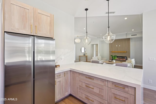 kitchen featuring hanging light fixtures, light brown cabinetry, stainless steel refrigerator, and kitchen peninsula