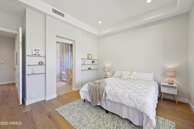 bedroom with a tray ceiling and light wood-type flooring