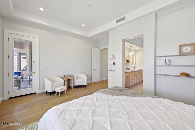 bedroom featuring connected bathroom, a raised ceiling, sink, and light hardwood / wood-style flooring