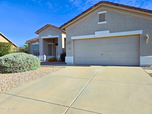view of front facade with an attached garage, driveway, a tiled roof, and stucco siding
