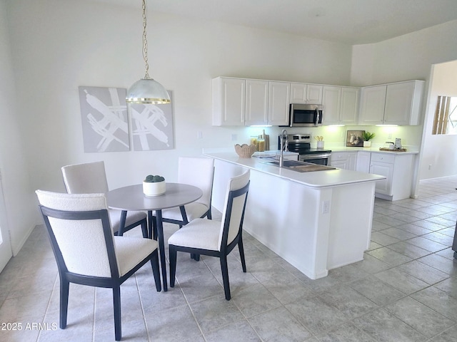 kitchen with light countertops, a sink, a peninsula, appliances with stainless steel finishes, and white cabinetry