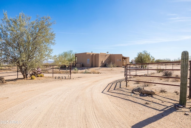 view of street with dirt driveway, a gated entry, and a rural view